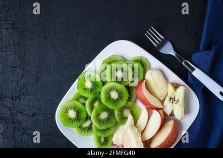 Dans une assiette sur une table en bois, mélanger des kiwis frais et des pommes avec des raisins. Banque D'Images