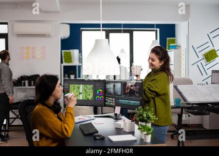 Collègues heureux parlant de montage de film regardant des films travaillant dans le bureau d'agence de création avec deux moniteurs. Les vidéastes traitent des projets vidéo dans des logiciels de post-production Banque D'Images