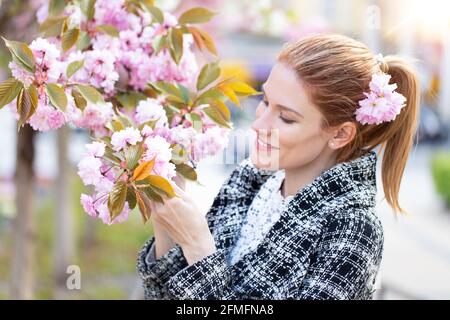 Jeune femme caucasienne à tête rouge tenant un portrait en fleur de cerisier Banque D'Images