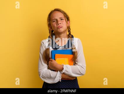 Fille pleure parce qu'il a beaucoup de devoirs à l'école. Expression émotionnelle. Arrière-plan jaune Banque D'Images