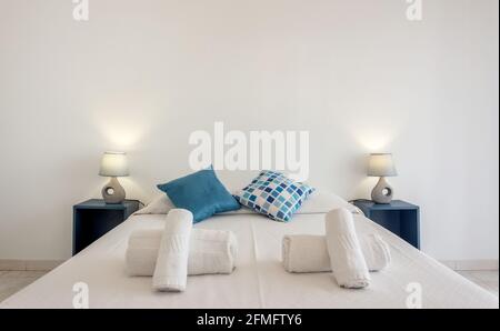 Chambre d'hôtel avec grand lit, avec quelques serviettes et oreillers sur le dessus. De chaque côté, il y a des tables de nuit avec des lampes. Banque D'Images