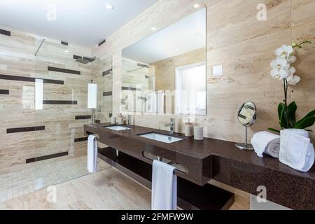 Salle de bains moderne grise carrelée avec lavabo donnant sur les toilettes et douche au bout de la chambre. Banque D'Images