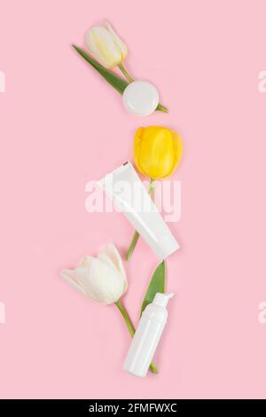 Saint-Valentin et Fête des femmes, concept de fête des mères. Vider les tubes et les bouteilles blancs avec des tulipes blanches sur fond rose. Flat lay, espace de copie. Banque D'Images