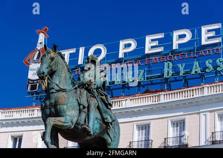 Puerta del sol dans le centre de Madrid, Espagne. Statue équestre du roi Charles III contre le signe emblématique de Tio Pepe le jour du ciel bleu ensoleillé Banque D'Images