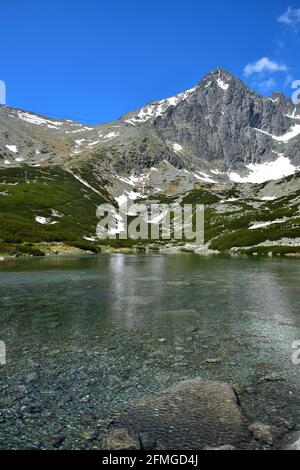 Un paysage dans les Hautes Tatras avec le lac clair Skalnate pleso et Lomnicky pic. Le petit téléphérique rouge sur son chemin vers le sommet est à peine à voir. S Banque D'Images