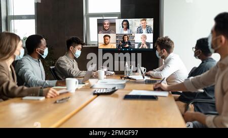 Divers hommes d'affaires dans des masques faisant des appels vidéo en ligne aux employés Banque D'Images