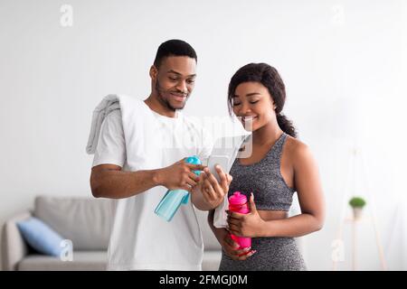 Couple afro-américain du millénaire prenant une pause de l'entraînement à domicile, regardant le tutoriel sportif en ligne sur le téléphone portable Banque D'Images