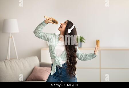 Femme indienne joyeuse avec un pinceau à cheveux pour chanter sa chanson préférée, porter un casque et danser à la maison Banque D'Images