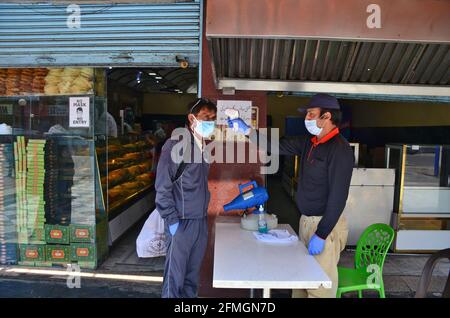 Srinagar, Inde. 09e mai 2021. Un travailleur vérifie la température d'un client avant d'entrer dans une boulangerie avant le festival musulman Eid al-Fitr lors d'un confinement imposé par les autorités à la suite de l'augmentation des cas de coronavirus à Srinagar. Alors que le mortel Covid-19 continue de menacer la vallée, les autorités ont prolongé dimanche le confinement actuel du COVID-19 devant le festival musulman Eid al-Fitr. Crédit : SOPA Images Limited/Alamy Live News Banque D'Images