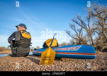 Kersey, CO, États-Unis - 29 janvier 2017 : un pagayer masculin senior se repose sur un gravelbar lors d'une promenade en pagayage sur la rivière South Platte, en mer froide Banque D'Images