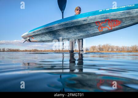 Fort Collins, Colorado, États-Unis - 24 mars 2020 : un pagayer masculin senior porte un tribord de course stand up paddleboard après l'entraînement de pagayage, au début du printemps Banque D'Images