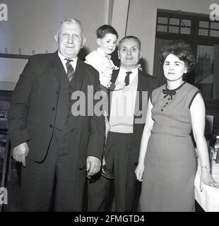 années 1960, historique, lors d'une fête d'anniversaire de mariage dorée, quatre générations d'une famille debout pour une photo. Nous voyons à gauche un arrière-grand-père, son fils, sa fille et le petit garçon de sa fille, qui est détenu par son père. Banque D'Images