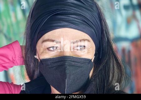 Portrait d'une jolie femme d'âge moyen de 50 ans avec des cheveux gris et masque de protection avec un mur de graffiti en arrière-plan Banque D'Images