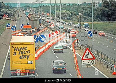 1981 image de paysage de transport d'archive regardant vers le bas sur les camions des années 1980 et les voitures dans les files d'attente de trafic lent en circulation dans le flux de contra Travaux routiers sur la section Newport Pagnell de la M1 autoroute avec panneaux d'avertissement de limite de vitesse et cônes séparant les lourdes Chariots de transport, y compris une vue arrière du camion MFI bande-annonce graphique d'un mobilier de détail historique populaire des années 80 Marque d'affaires avec humoristique ou peut-être mal humour slogan ont Un jour de Nice comme nous avons eu une vue d'archives Buckinghamshire Angleterre Royaume-Uni Banque D'Images