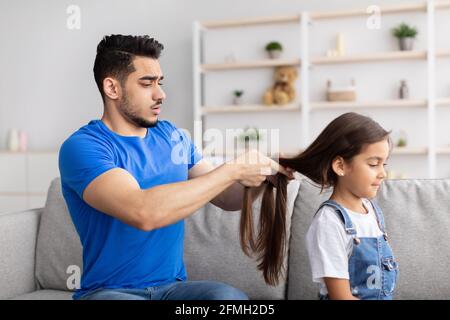 Père faisant une tresse de cheveux pour fille assise sur un canapé Banque D'Images