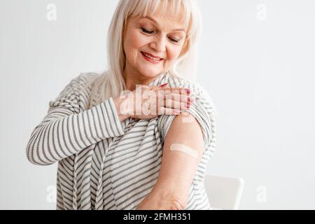 Femme âgée présentant un bras vacciné après une injection d'antiviral, mur blanc Banque D'Images