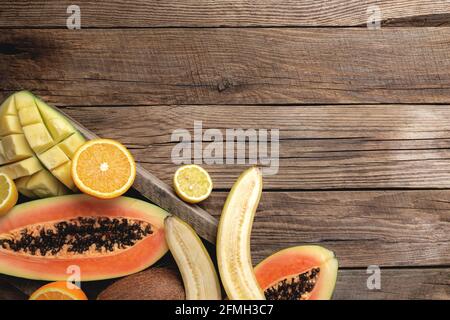 Fruits tropicaux frais dans une boîte de livraison en bois sur fond de bois. Papaye, orange, banane, noix de coco, mangue, kiwi et citron vue sur le dessus, plat avec c Banque D'Images