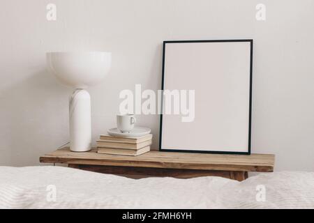 Une tasse de café sur une pile de livres et une lampe géométrique en marbre moderne. Maquette verticale noire de cadre d'image sur banc, table vintage. Fond de mur blanc Banque D'Images