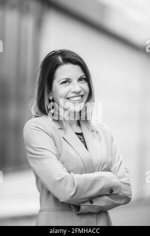 Prise de vue verticale en niveaux de gris d'une jeune femme qui se pose un costume gris aux bras croisés Banque D'Images