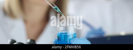 Une scientifique féminine goutte du liquide bleu de la pipette dans le flacon laboratoire Banque D'Images