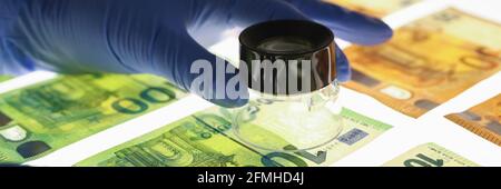 Mains dans des gants en caoutchouc tenant la loupe avec les billets de banque Banque D'Images