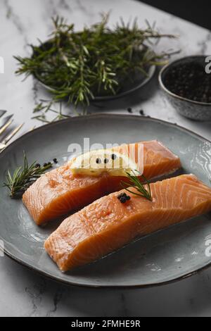 Un cliché vertical de deux filets de saumon servis sur un assiette avec citron et romarin sur la table Banque D'Images