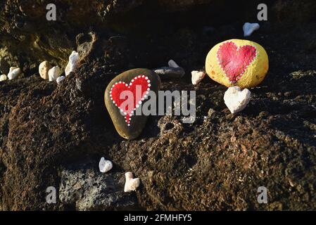 Corail et pierres en forme de cœur, peints de coeurs « amoureux » rouge vif, placés dans des roches volcaniques sur le rivage à Sandy Beach Park, Oahu, Hawaii, États-Unis Banque D'Images