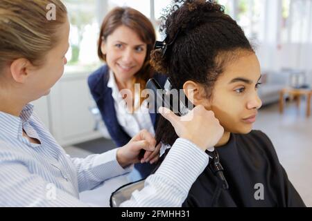 coiffeur stagiaire à l'aide d'un dispositif de lissage sur les cheveux bouclés Banque D'Images