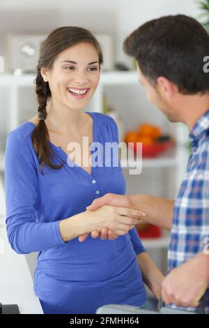 homme réparateur se serrant la main avec une jeune femme heureuse dans la cuisine Banque D'Images