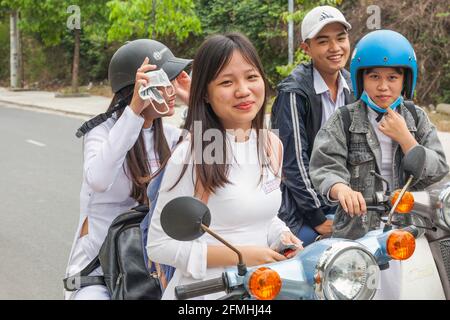Les écolières vietnamiennes portant la robe nationale ao dai quittent l'école à moto, Hoi an, Vietnam Banque D'Images