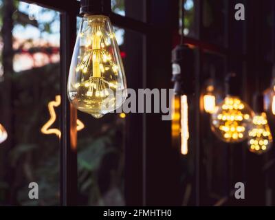 Décoration d'ampoule dans le café. De nombreuses lampes LED de style rétro brillent dans l'arrière-plan sombre près de la fenêtre en verre. Banque D'Images