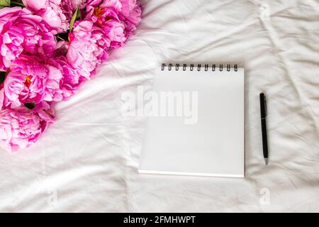 Ouvrez un bloc-notes vierge sur la spirale sur fond de coton clair et bouquet de fleurs de pivoines roses. Banque D'Images