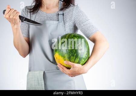 Une femme caucasienne se prépare à stab une pastèque à l'aide d'un couteau de cuisine aiguisé. Une image polyvalente pour les fruits d'été ainsi qu'une démonstration de for Banque D'Images