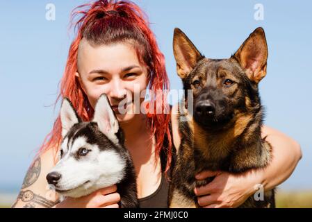 Content athlète féminine avec piercing embrassant Husky sibérien et allemand Shepherd tout en regardant l'appareil photo au soleil Banque D'Images