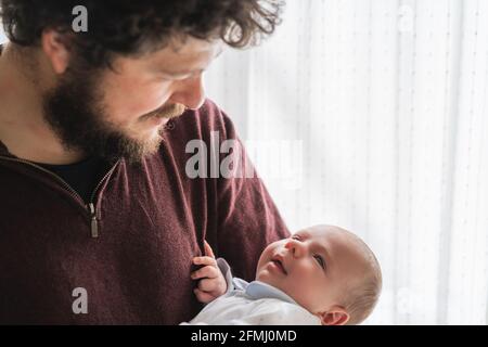 Papa barbu adulte avec des cheveux bouclés en cuddling mignon petit enfant se regardant les uns les autres dans la maison Banque D'Images