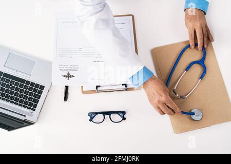 Vue de dessus de la récolte un homme méconnaissable qui travaille à la table avec papier et netbook contre le stéthoscope dans l'hôpital Banque D'Images