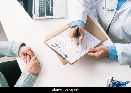Un médecin masculin âgé non reconnaissable a été mis en culture sous forme uniforme sur la planchette à pince de la table contre une femme méconnaissable pendant le contrôle clinique Banque D'Images