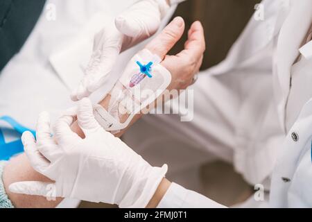 Grand angle de la récolte anonyme medic dans les gants jetables de mise cathéter intraveineux sur le bras du patient à l'hôpital Banque D'Images