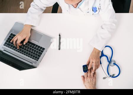 Vue de dessus de la récolte méconnaissable médecin mesurant l'oxygène du sang de patient avec moniteur de fréquence cardiaque à la table avec stéthoscope dans clinique Banque D'Images