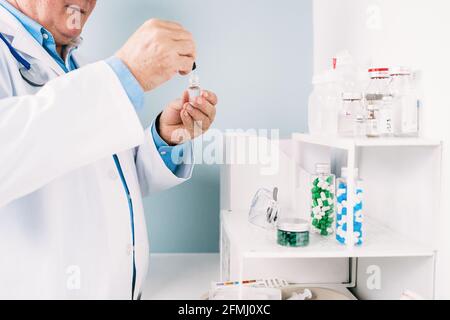 Vue latérale d'un homme âgé non reconnaissable en culture, médecin verres uniformes et protecteurs avec compte-gouttes et flacon avec liquide à l'hôpital Banque D'Images