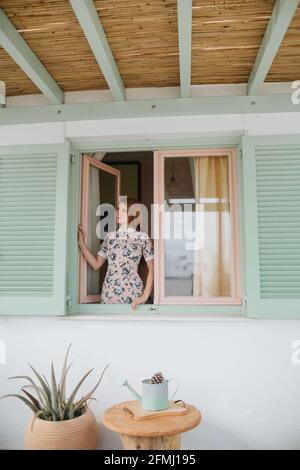 Belle jeune femme en été vêtements debout près de la maison contemporaine et la recherche Banque D'Images