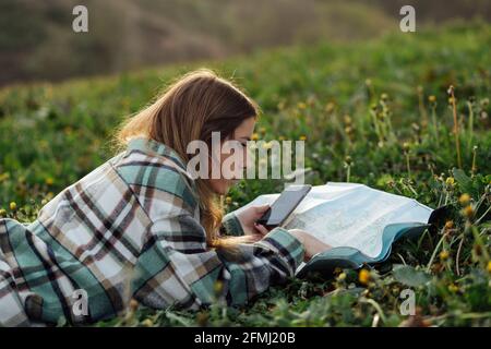 Vue latérale d'une jeune femme touristique avec un téléphone portable pour regarder la route carte en étant couché sur l'herbe dans la campagne Banque D'Images