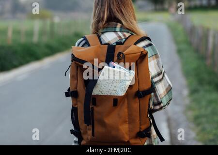 Vue arrière de crop anonyme femelle randonneur avec carte d'itinéraire dans un sac à dos sur la route en campagne Banque D'Images