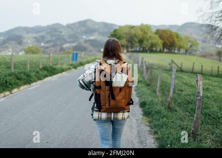 Vue arrière du randonneur anonyme avec carte d'itinéraire dans sac à dos roulant sur la route de campagne contre le mont Banque D'Images