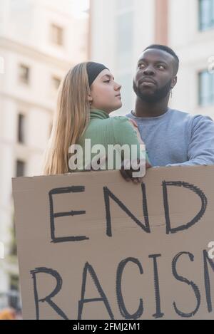 Couple multiracial s'embrassant dans la rue de la ville tout en protestant avec la fin Affiche sur le racisme pendant la démonstration de Black Lives Matter Banque D'Images