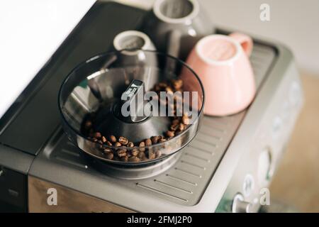 Du dessus des grains de café torréfiés dans le moulin électrique contre tasses en céramique sur le support de la machine à espresso moderne à la maison Banque D'Images