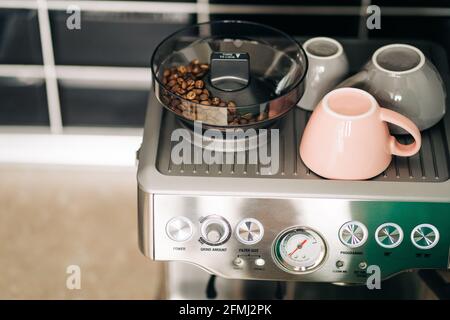 Du dessus des grains de café torréfiés dans le moulin électrique contre tasses en céramique sur le support de la machine à espresso moderne à la maison Banque D'Images