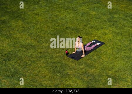 De dessus de jeune femme dans les vêtements de sport exécutant Urdhva Mukha Svanasana pose tout en pratiquant le yoga sur la pelouse Banque D'Images