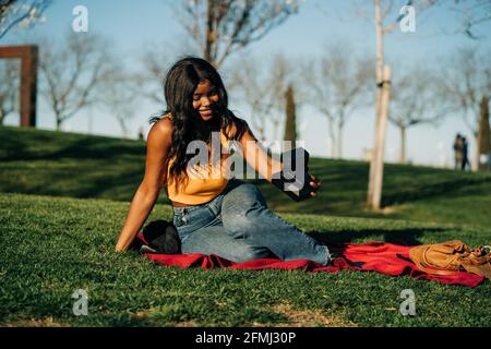 Une femme afro-américaine ravie de prendre sa photo sur un instant rétro appareil photo tout en étant assis sur une couverture dans le parc en été soirée Banque D'Images