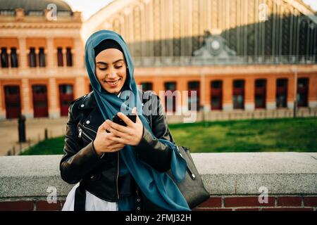 Femme musulmane en foulard traditionnel debout dans la rue de la ville et navigation dans le téléphone Banque D'Images
